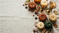 Autumn harvest composition with colorful pumpkins, golden candles, cinnamon sticks, star anise and dried leaves on neutral linen background for seasonal decor.