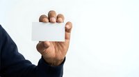 Close-up of male hand with medium skin tone holding blank white business card against white background, suitable for corporate branding and contact information design.