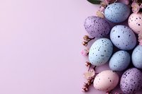 Pastel speckled Easter eggs in blue, pink and purple shades decorated with delicate spring blossoms on soft pink background with copy space for seasonal designs.