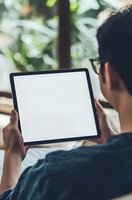 Asian male professional wearing glasses holds tablet device with blank white screen while working remotely outdoors in natural setting.