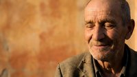Senior man with weathered facial features and gray hair smiling warmly against warm-toned textured background. Suitable for healthcare, aging, wisdom, lifestyle and portrait projects.