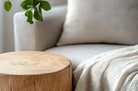 Natural wood stump side table with visible tree rings next to cozy white sofa and green plant leaves, creating minimalist scandinavian living room atmosphere.
