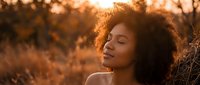 Young African American woman with curly hair enjoying peaceful moment in golden sunset light outdoors during autumn season for wellness and mindfulness concepts.