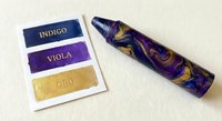Colorful acrylic paint tubes with purple and gold swirls alongside color sample cards showing indigo, viola, and oro shades for artistic projects.