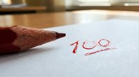 Red pencil marking 100 score on white paper in classroom setting for academic achievement and educational success concepts.
