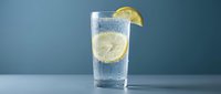Refreshing glass of sparkling water with fresh lemon slices and ice cubes on blue background, perfect for beverage, wellness and hydration concepts.