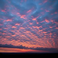 Dramatic sunset sky with vibrant pink and orange clouds scattered across deep blue heavens creating stunning natural light display for backgrounds.