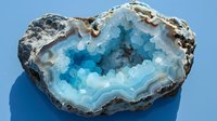 Stunning blue agate crystal geode slice with natural layered formation and crystalline interior structure on gray background, macro mineral photography.