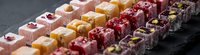 Assorted gourmet Turkish delight confections with nuts, rose petals and fruit flavors arranged in colorful rows on dark slate surface for dessert menu.