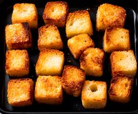 Golden crispy potato cubes roasted to perfection, showing caramelized edges and tender centers arranged on dark surface, macro food photography.