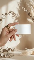 Female hand holding blank white business card with golden jewelry in warm sunlight with botanical shadow overlay for branding mockup.