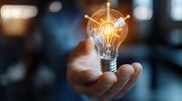 Glowing light bulb floating above open palm with digital network connections, symbolizing innovation and creative business solutions on blurred background.