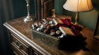 Assorted chocolates and truffles in decorative box on wooden dresser with lamp and vintage decor, luxury confectionery gift styling.