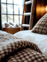 Cozy bedroom interior with brown plaid blanket and white bedding, wooden ladder and wicker basket near window creating warm autumn atmosphere for lifestyle design.