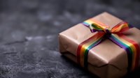 Gift box wrapped in rose gold paper with rainbow pride ribbon bow on dark textured background, selective focus. Perfect for LGBTQ celebration and special occasions.