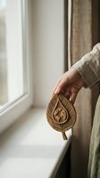 Person holding carved wooden leaf ornament by window with natural light and neutral interior decor for home styling and mindfulness concepts.