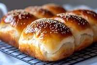 Freshly baked soft milk bread rolls with sesame seeds on cooling rack, showing golden brown crust and fluffy texture. Close up view of homemade Japanese style bread.