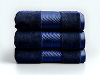 Stack of three folded navy blue luxury cotton bath towels with decorative textured border stripe against white background, soft hotel spa quality linens.
