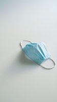 Disposable surgical mask with blue pleated design and white elastic ear loops on neutral background, suitable for healthcare, medical, safety, and pandemic-related projects.