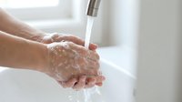 Hands washing with soap under running water from modern faucet in clean bathroom sink for hygiene and health protection against germs and bacteria.