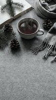 Cozy winter flatlay with steaming tea cup, pine cones, fir branch, open book and gray scarf on soft textile background with copy space.