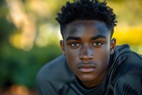 Young African American man with curly hair in black hoodie outdoors with warm golden hour lighting and natural bokeh background.