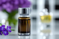 Small brown glass bottle with silver cap against blurred background with purple flowers, suggesting natural aromatherapy or essential oil product photography.