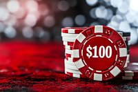 Stack of red and white casino poker chips with $100 denomination on red velvet surface against blurred bokeh background, dramatic lighting highlights gaming atmosphere.
