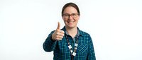 Young adult male with light skin tone and brown hair wearing eyeglasses and a teal plaid shirt, giving thumbs up gesture with a friendly smile against white background.