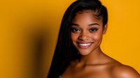 Young African American woman with bright smile and long straight black hair against vibrant yellow background, beauty portrait showcasing natural makeup and glowing skin.