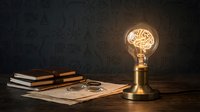 Light bulb with glowing brain filament on wooden desk with vintage books and magnifying glass symbolizing creative thinking and knowledge innovation.