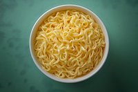 Fresh cooked instant ramen noodles in white ceramic bowl on green background, top view of traditional Asian fast food meal preparation.