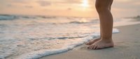 Close-up of bare feet walking on sandy beach at sunset with gentle waves washing shore. Peaceful coastal scene for wellness and vacation concepts.
