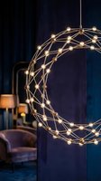Modern geometric pendant light fixture with interconnected brass spheres and glowing bulbs suspended in dark interior space with velvet furniture and curtains for contemporary home decor.