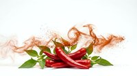 Fresh red chili peppers with green leaves and spice powder explosion on white background, vibrant food concept for culinary design.