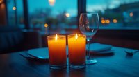 Romantic dinner setting with glowing orange candles and empty wine glass on wooden table against blurred city lights background at dusk, creating intimate ambiance.
