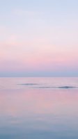 Serene coastal seascape at dawn with soft pink and blue tones reflecting on calm ocean waters and gentle waves for peaceful nature backgrounds.