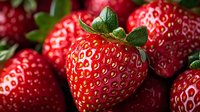 Fresh ripe strawberries with vibrant red color and natural texture closeup. Green leaves and yellow seeds visible on juicy berries surface in macro photography.