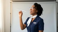 African American female flight attendant in navy uniform holding paper airplane with joyful expression for aviation and travel industry concepts.
