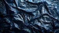 Dark blue crumpled plastic bag texture with dramatic shadows and highlights creating abstract pattern. Moody atmospheric background for creative projects.