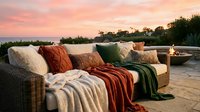 Outdoor wicker sofa with colorful pillows and blankets on a wooden deck at sunset, perfect for patio and garden design projects.