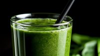 Fresh green smoothie with spinach, kale and healthy ingredients in glass on dark background. Nutritious detox drink with black straw.