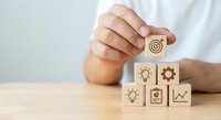 Male professional hand placing wooden cube with target icon completing business strategy pyramid on desk representing goal achievement and success planning.