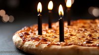 Fresh baked pizza with burning black candles on dark background, celebrating birthday or anniversary with unique pizza party concept.