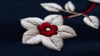 Delicate embroidered flower with white petals and red center on dark navy fabric, featuring intricate stitching details and dimensional needlework texture.