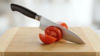 Chef's knife with black handle slicing fresh red tomato on wooden cutting board, food preparation and cooking concept.