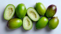 Fresh green jujube fruits whole and cut in half showing white flesh and seeds on white background, organic healthy tropical produce for eating raw.