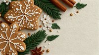 Festive gingerbread snowflake cookies decorated with white icing, surrounded by pine branches, cinnamon sticks, and star anise on beige background.