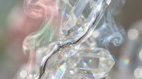 Colorful smoke swirls around sparkling crystal prisms creating magical light refractions and rainbow effects on blurred background for creative designs.