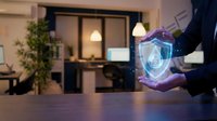 Businessperson holding glowing digital shield with biometric scan in modern office workspace, representing cybersecurity and data protection technology solutions.